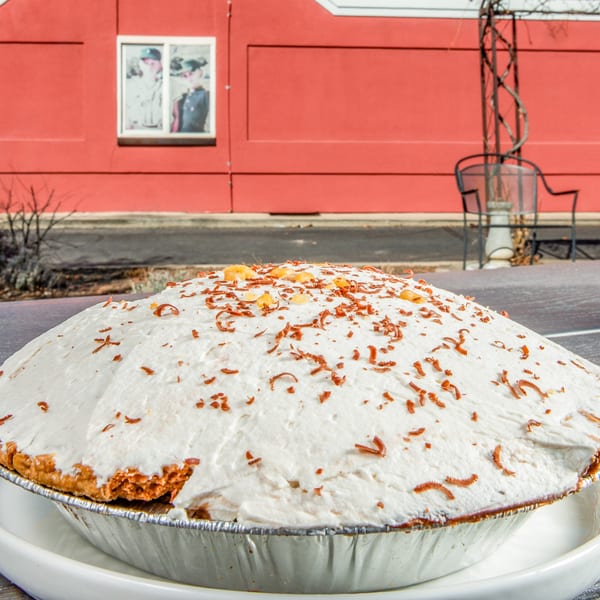 A large pie with white whipped topping and chocolate shavings sits outdoors on a table.