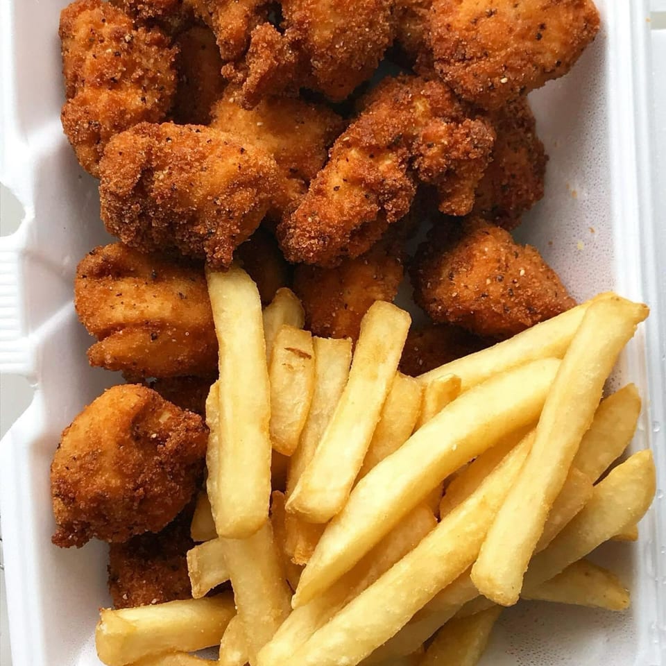 Golden-brown fried chicken nuggets and crispy french fries in a white takeout container.
