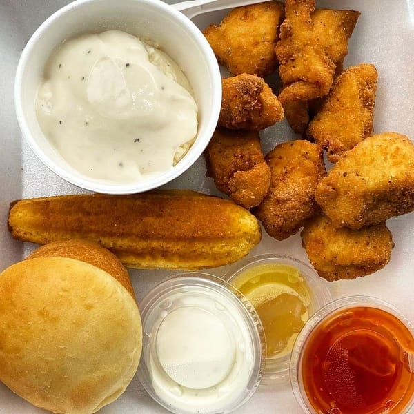 C & B Famous Chicken meal with fried chicken nuggets, mashed potatoes, cornbread, roll, and sauces.